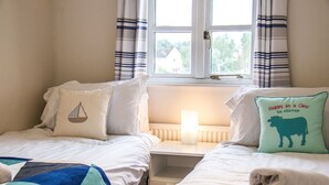 A cozy bedroom with two beds, a bedside table with a lamp, and a window with curtains. - Windrush Lake 88, Waterside - Lakeside Lodge, On-site Activities, Sleeps 8 (SOUTH CERNEY)