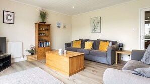 A living room with a sofa, coffee table, bookshelf, and a framed letter on the wall, and a radiator. - Windrush Lake 88, Waterside - Lakeside Lodge, On-site Activities, Sleeps 8 (SOUTH CERNEY)