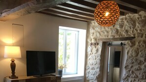 Una sala de estar acogedora con una pared de piedra, un banco de madera, un televisor y una lámpara.