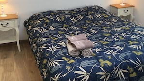 Un dormitorio con una cama cubierta por un edredón estampado con motivos florales, dos mesitas de noche con lámparas y suelo de madera.
