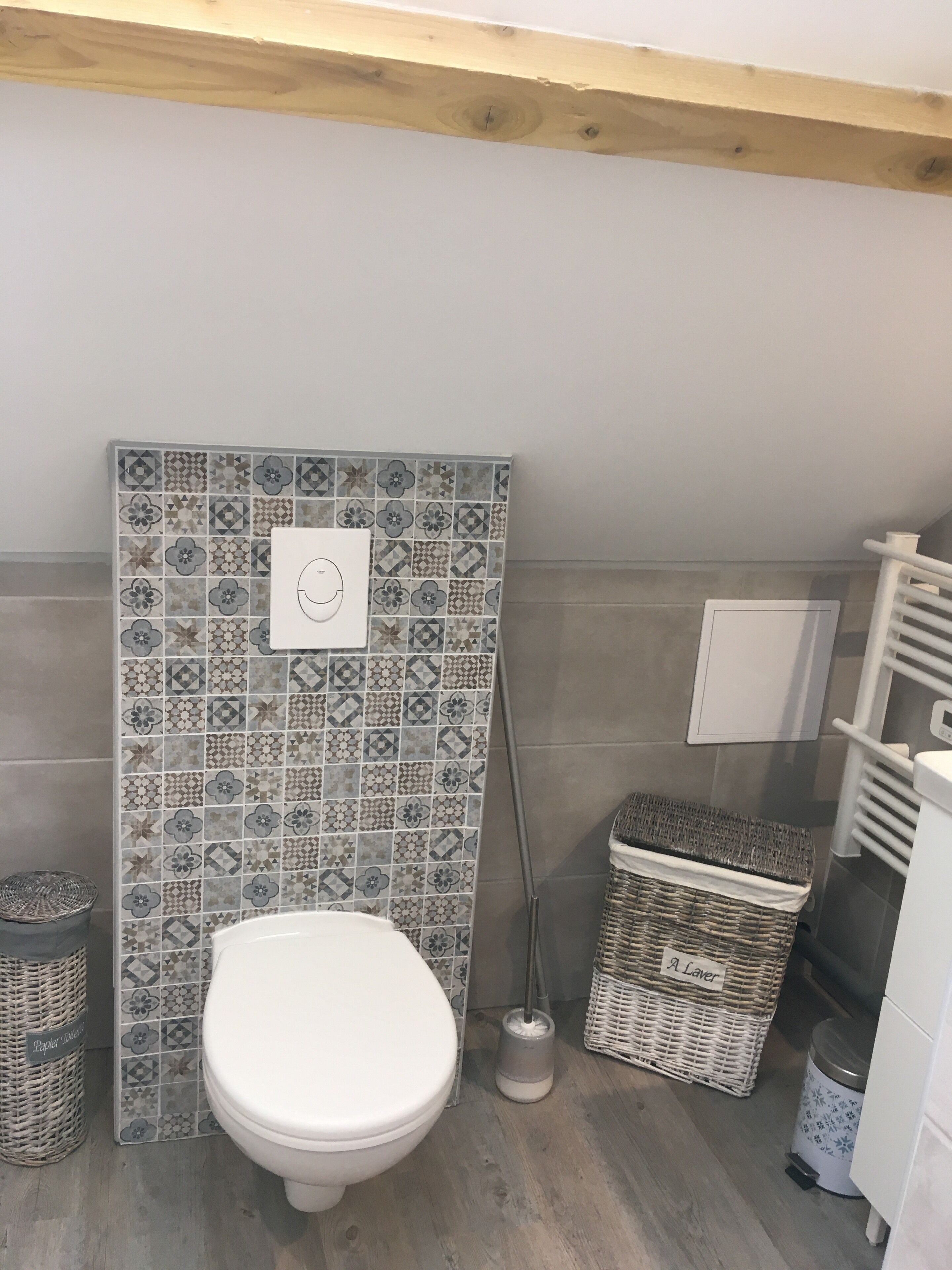 A bathroom with a white toilet, patterned tiles, wicker baskets, and a white towel rack.