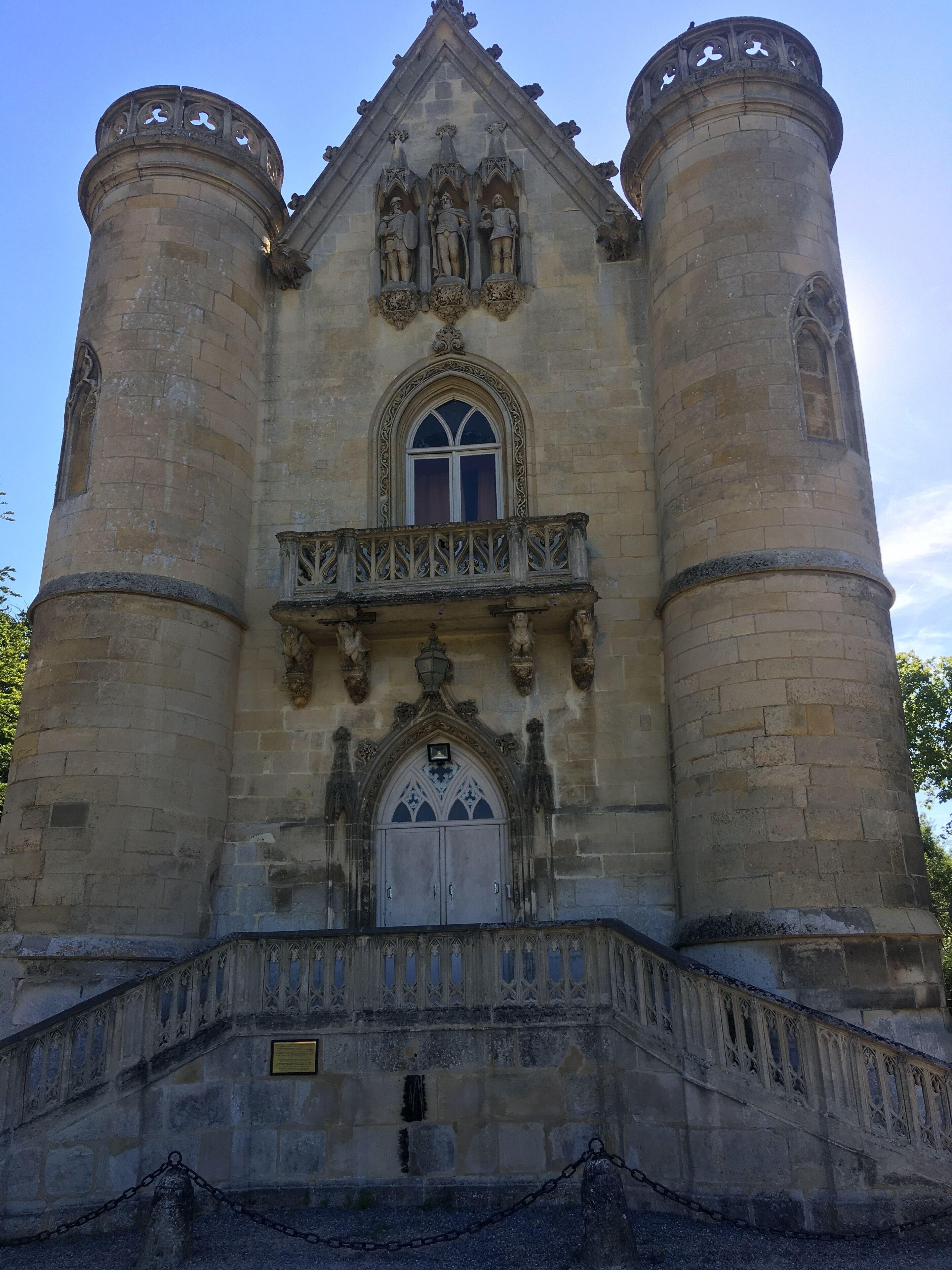Un bâtiment historique doté d’une fenêtre centrale en arc de cercle, de deux tours de chaque côté et d’un balcon orné de sculptures complexes en pierre.