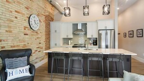 A modern kitchen with a central island, bar stools, a black leather chair, and a clock on the wall.