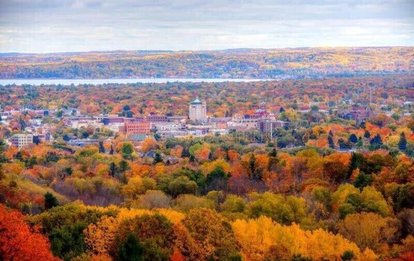 A panoramic view of a town with autumn foliage, buildings, and a lake in the background. - Golden Lofts Unit 1 Downtown Traverse City 1BD/1BA (Traverse City)