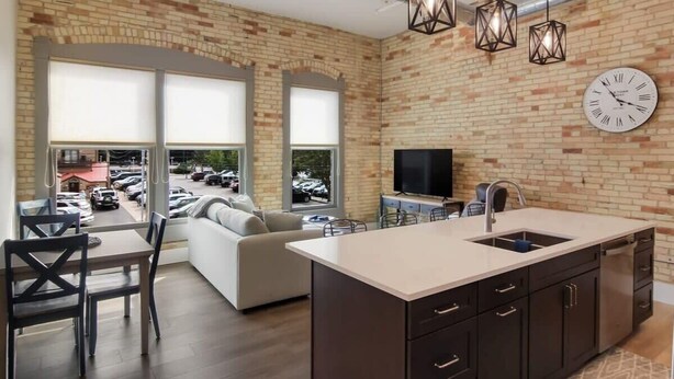 A modern kitchen with a large island, a dining area with a sofa, and a large window overlooking a parking lot.