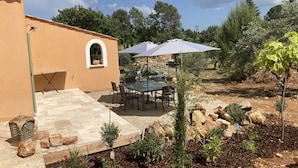 Une terrasse avec une table et des chaises, entourée d’un jardin où poussent différentes plantes et un petit arbre.