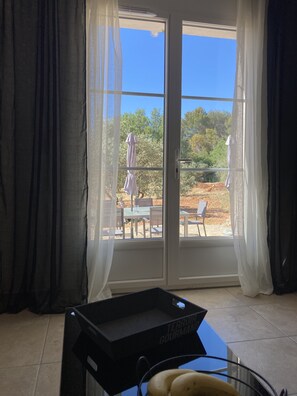 Een kamer met een schuifglasdeur die uitkomt op een buitengebied met tafels en stoelen.