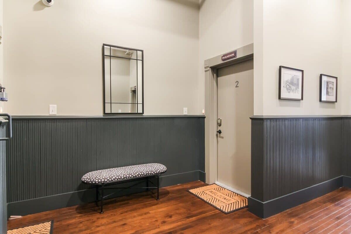 Un couloir avec un banc, une porte portant l’inscription « 2 », un miroir et deux tableaux encadrés accrochés au mur.
