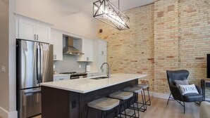 A modern kitchen with a central island, stainless steel appliances, and a brick accent wall. - Golden Lofts Unit 3 Downtown Traverse City 2bd/2ba (Traverse City)