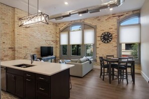 Una cocina moderna con una isla central, un comedor con mesa y sillas, un sofá y un amplio ventanal con persianas.