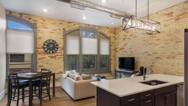 Une cuisine moderne avec un îlot central, un coin repas comprenant une table et des chaises, un canapé et une grande horloge au mur.
