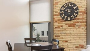 Un coin repas avec un mur en briques, une grande horloge et une fenêtre donnant sur un immeuble.