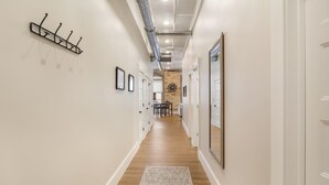 Un couloir avec un plancher en bois, des murs blancs, un porte-manteau, des tableaux encadrés et une porte au fond.