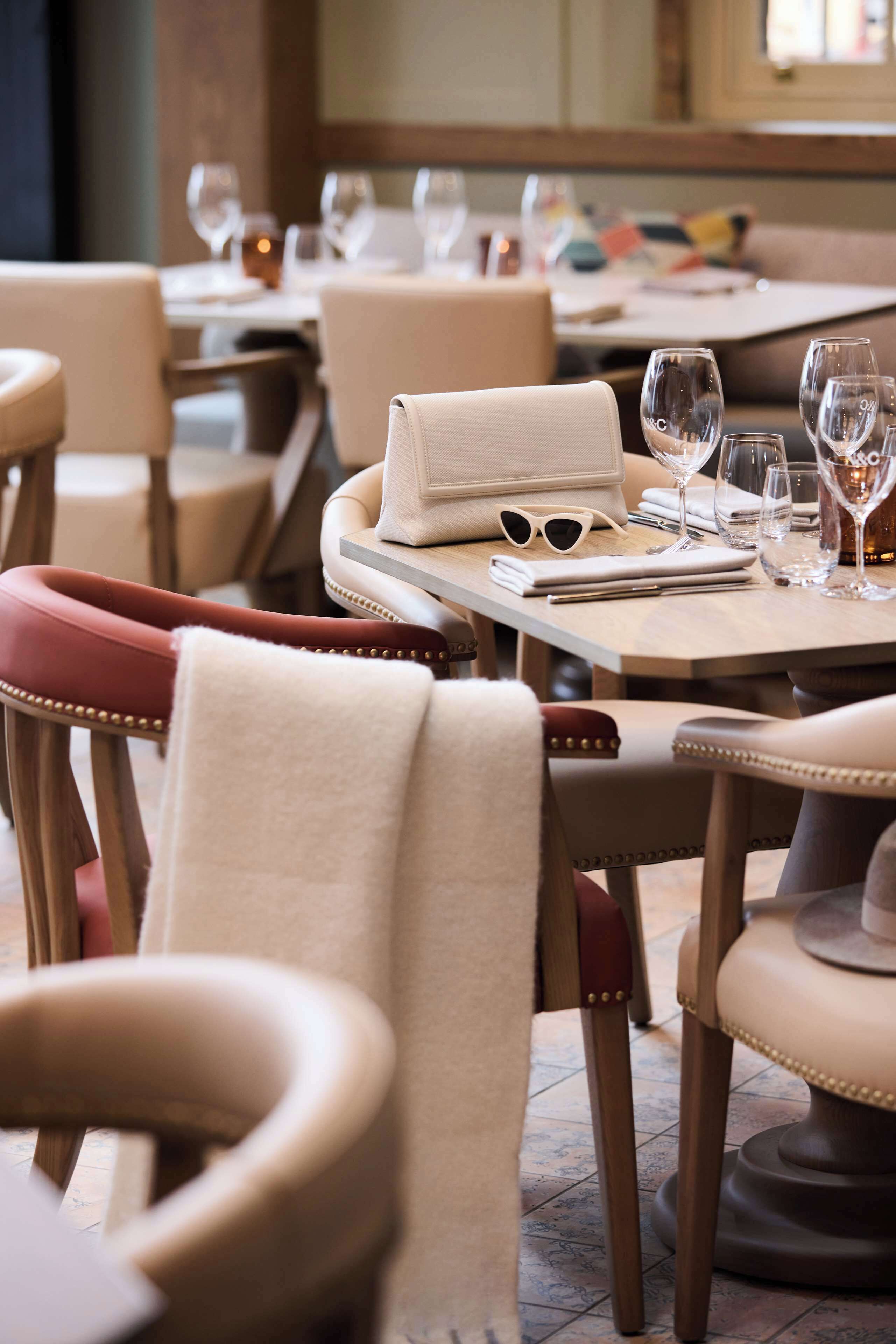A restaurant interior with leather chairs, a table set with wine glasses, a handbag, and sunglasses.