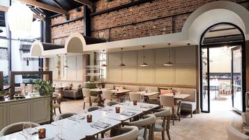 Un restaurante amplio con techos altos, paredes de ladrillo visto y una variedad de opciones de asientos, incluyendo mesas y cabinas.