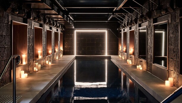 A modern indoor pool with a geometric light installation, stone walls, and a minimalist design. - Adina Apartment Hotel Melbourne Pentridge (Coburg)