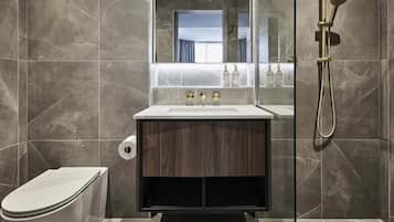 Et moderne badeværelse med en væg belagt med marmorfliser, en trækommode, et hvidt toilet og et bruseområde med glasvægge.