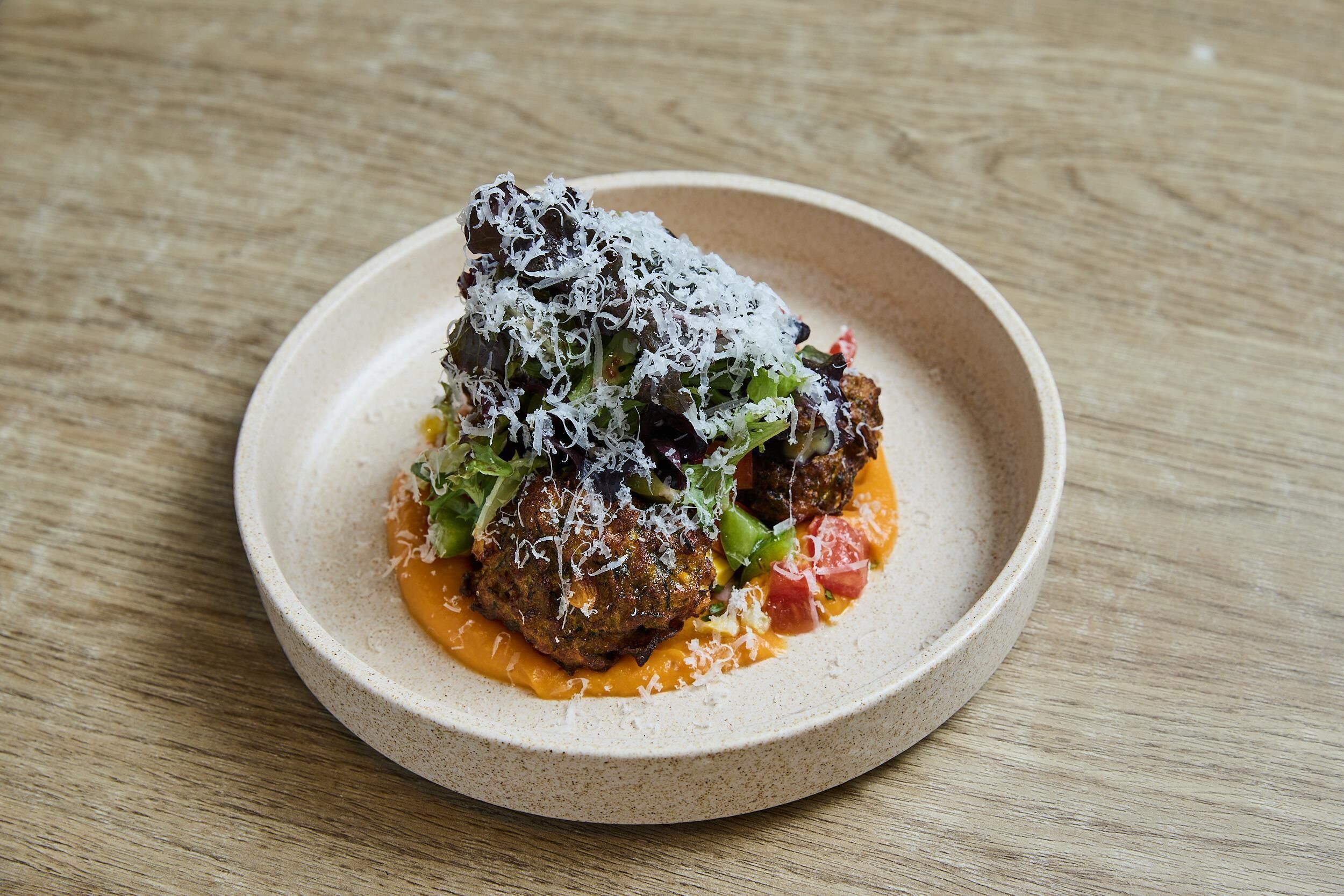 A plate of food with meatballs, cheese, and vegetables on a wooden table.