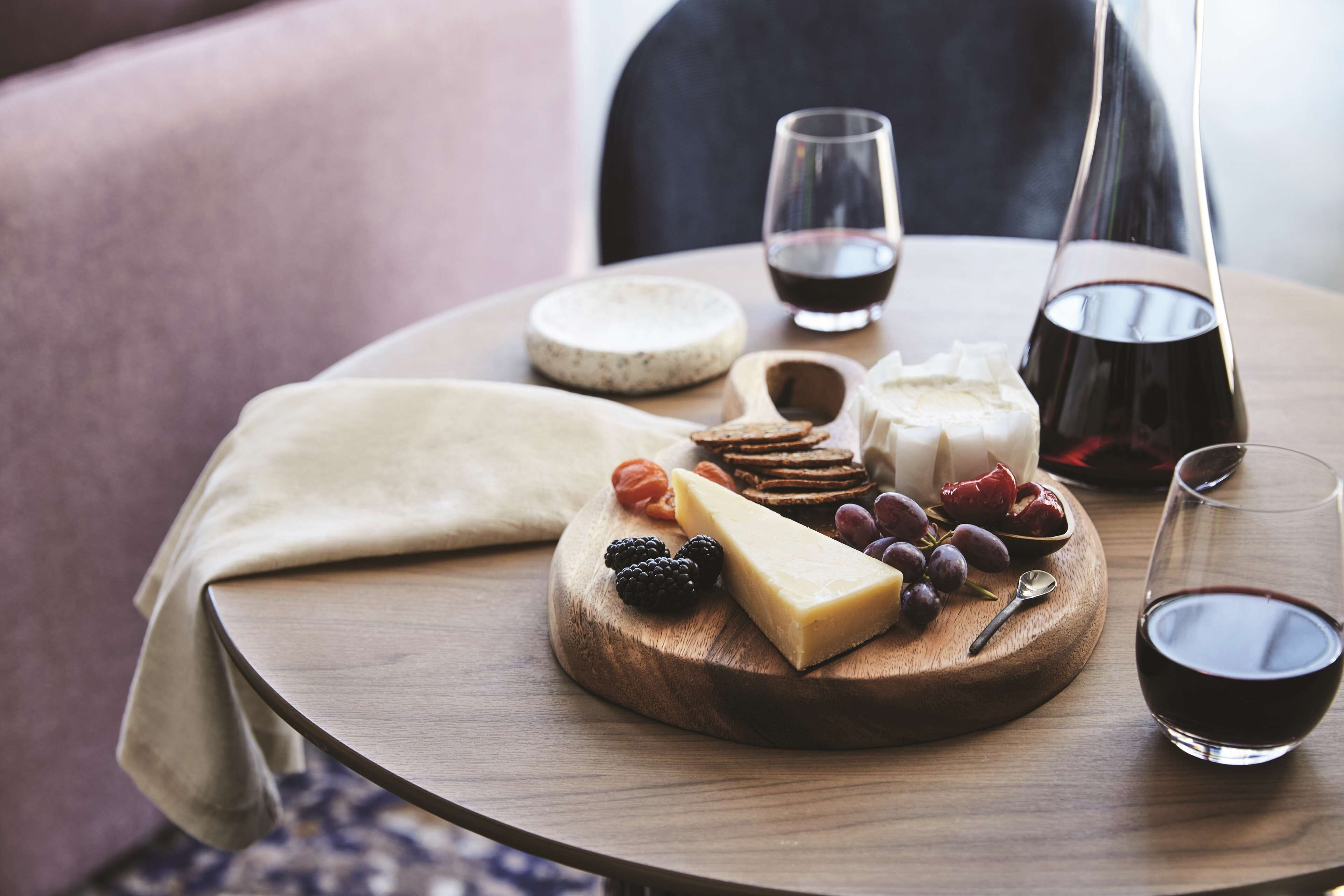 A wooden board with cheese, fruits, and crackers on a table.
