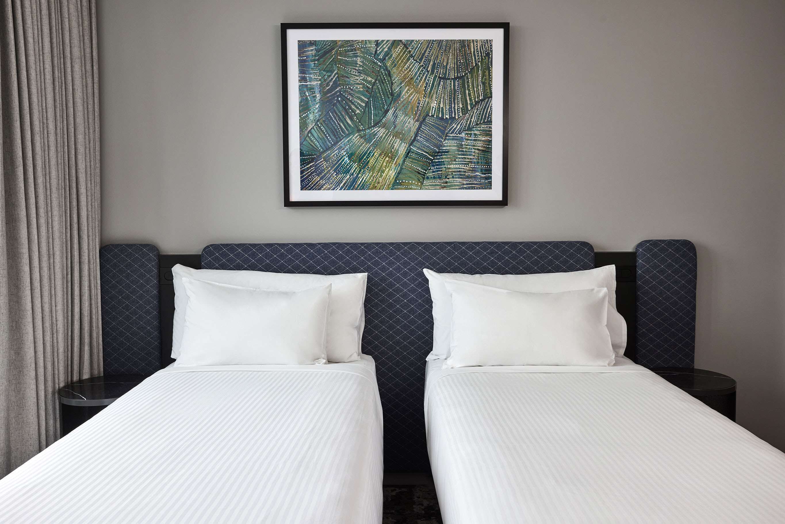 Una habitación de hotel con dos camas, una obra enmarcada en la pared y un cabecero de diseño oscuro.