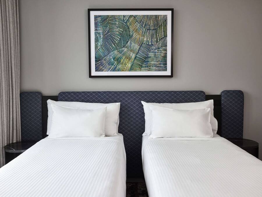 Una habitación de hotel con dos camas, una obra enmarcada en la pared y un cabecero de diseño oscuro.