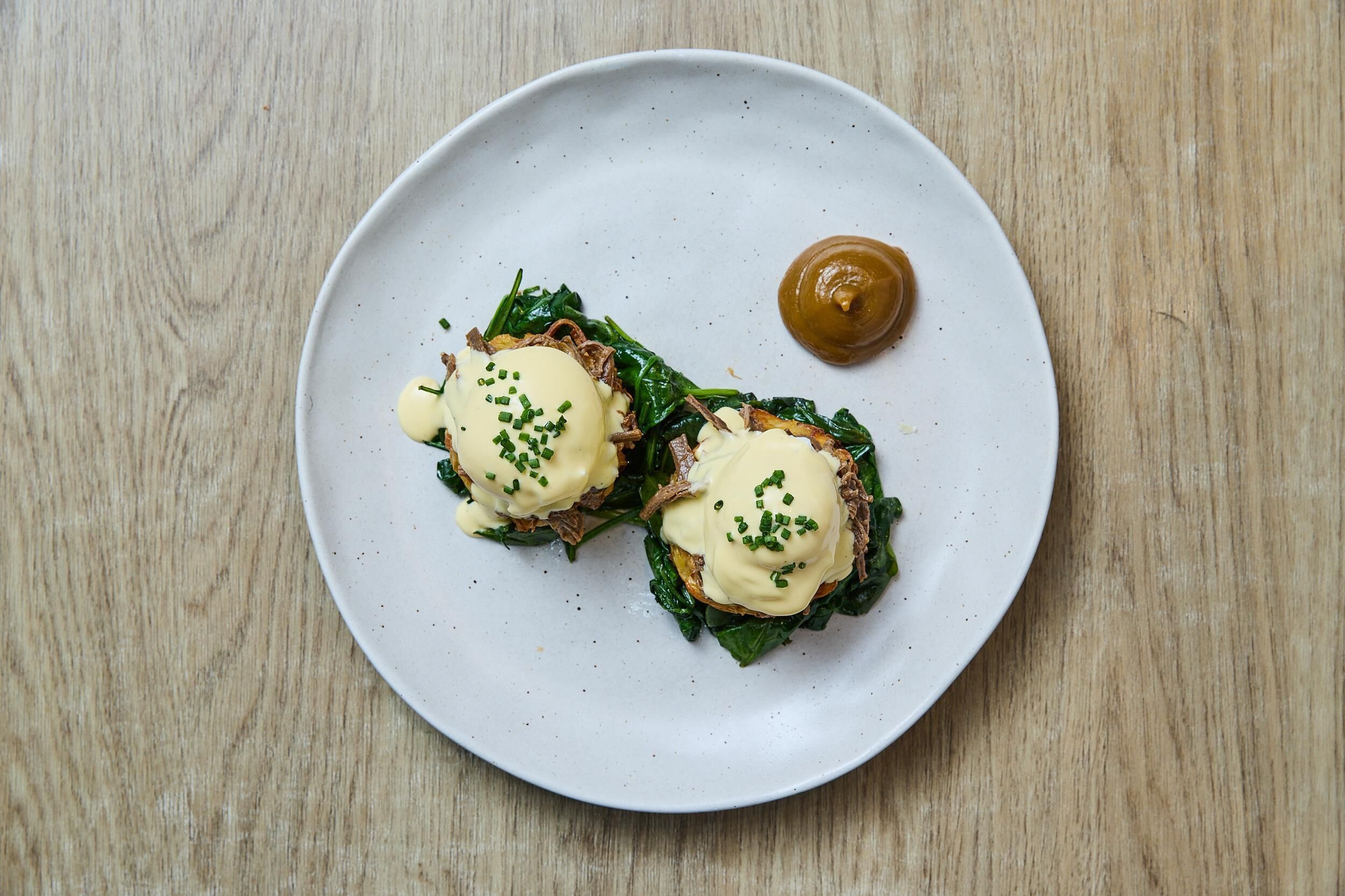 A plate with two eggs benedict sandwiches and a dollop of sauce on a wooden table.