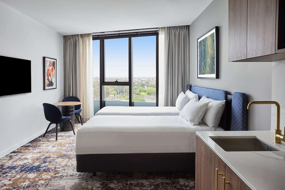 Una habitación de hotel con un ventanal grande, una cama, un escritorio y un lavamanos.
