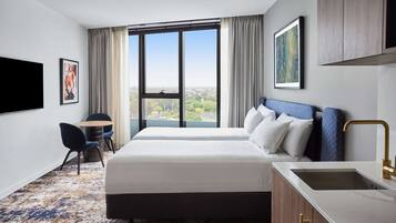 A hotel room with a large window, a bed, a desk, and a sink.