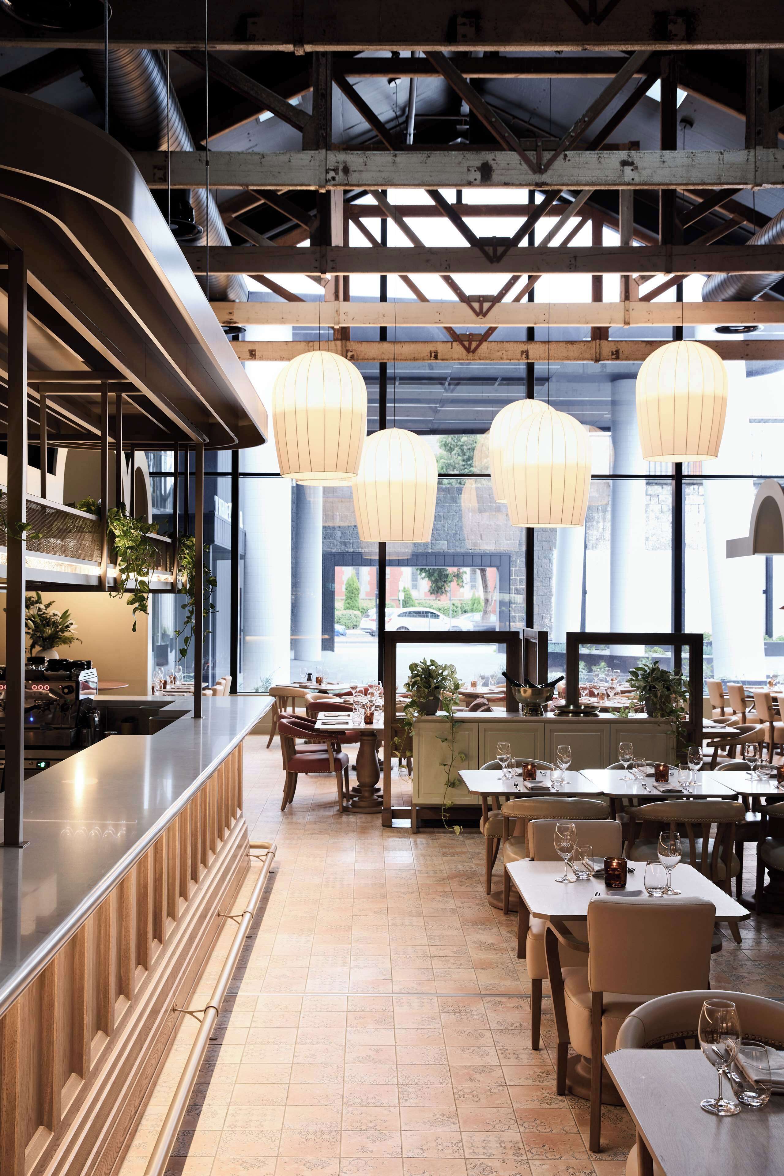 A restaurant with a long counter, multiple tables, hanging light fixtures, and large windows.