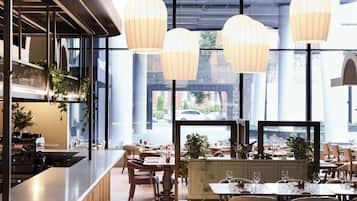 A restaurant with a long counter, multiple tables, hanging light fixtures, and large windows.