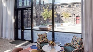 A modern hotel lobby with large windows, a stone wall, and a seating area with a patterned rug. - Adina Apartment Hotel Melbourne Pentridge (Coburg)
