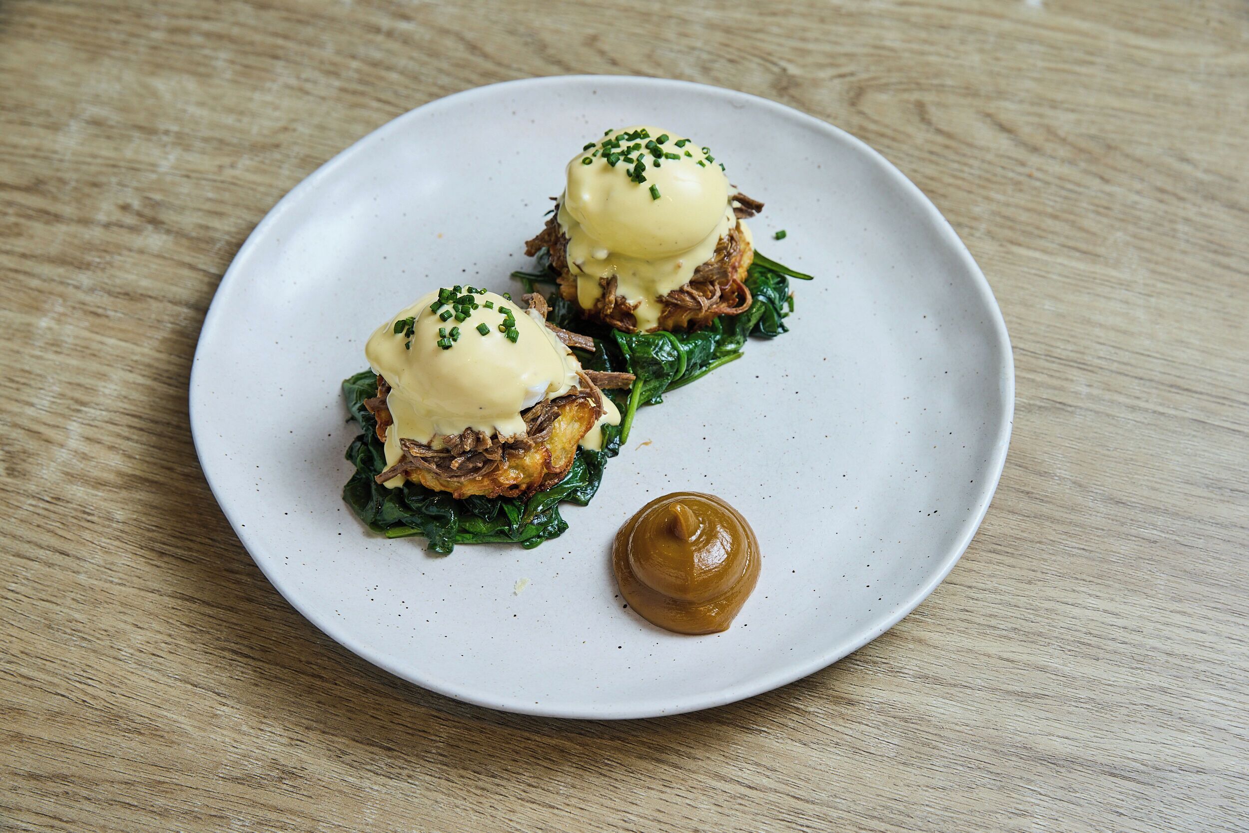 A plate with two poached eggs on a bed of greens and meat, and a dollop of sauce on a white plate.