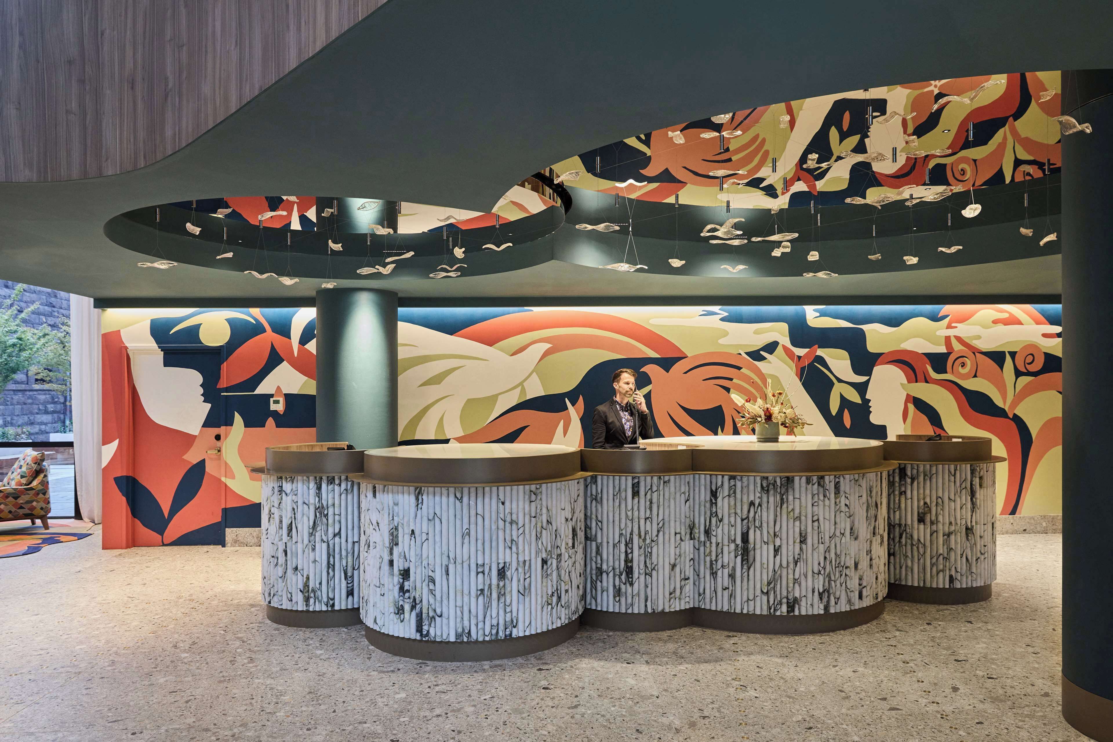 A reception area with a curved counter, a large abstract mural, and hanging light fixtures.