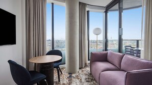 A modern hotel room with a large window, a round table, a purple sofa, and a TV mounted on the wall. - Adina Apartment Hotel Melbourne Pentridge (Coburg)