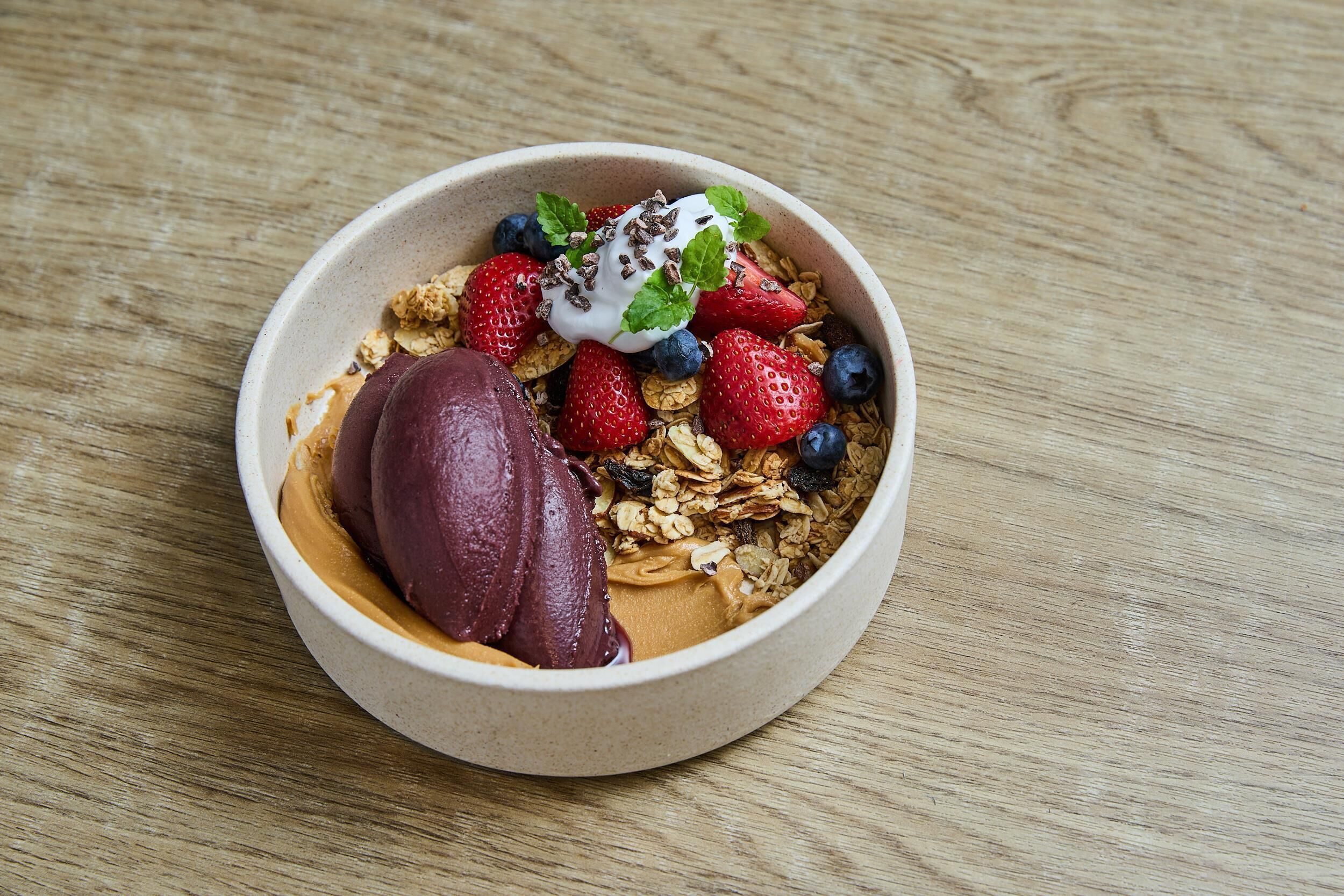 Un tazón de cereal con fresas, arándanos y una cucharada de yogur sobre una superficie de madera.