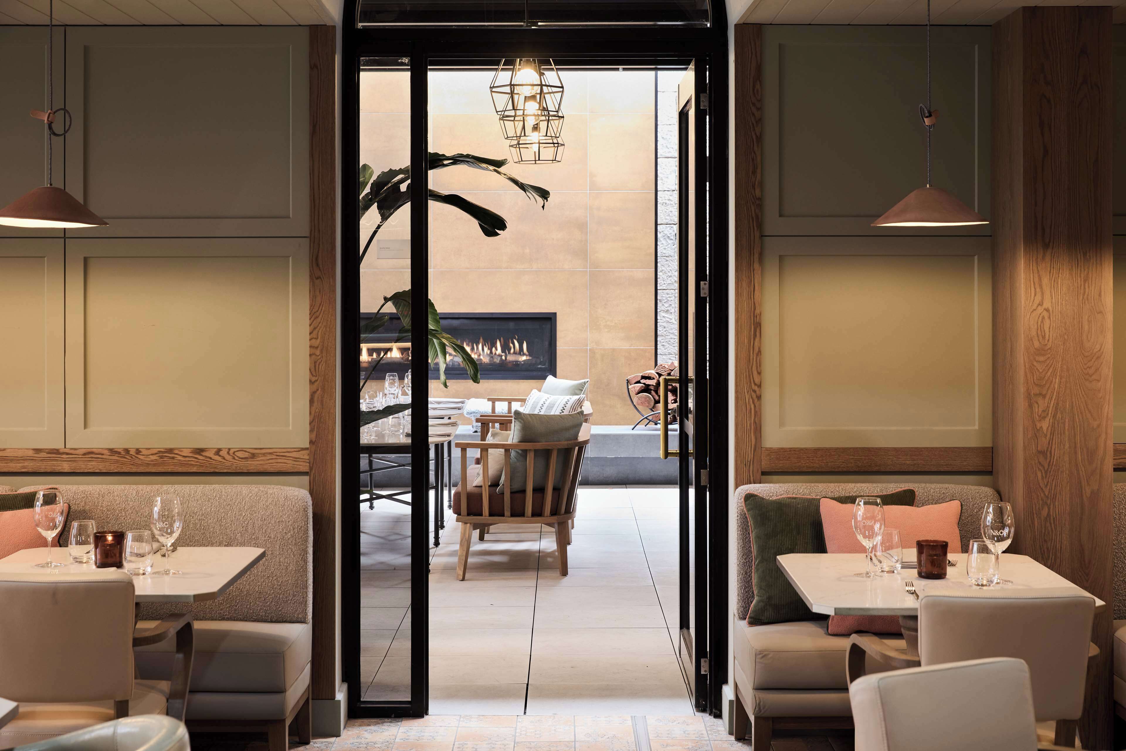 Un restaurant au décor moderne, avec une salle à manger centrale agrémentée d’une cheminée, de meubles en bois et de luminaires suspendus.