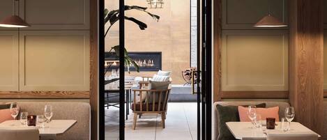 Un restaurant au décor moderne, avec une salle à manger centrale agrémentée d’une cheminée, de meubles en bois et de luminaires suspendus.