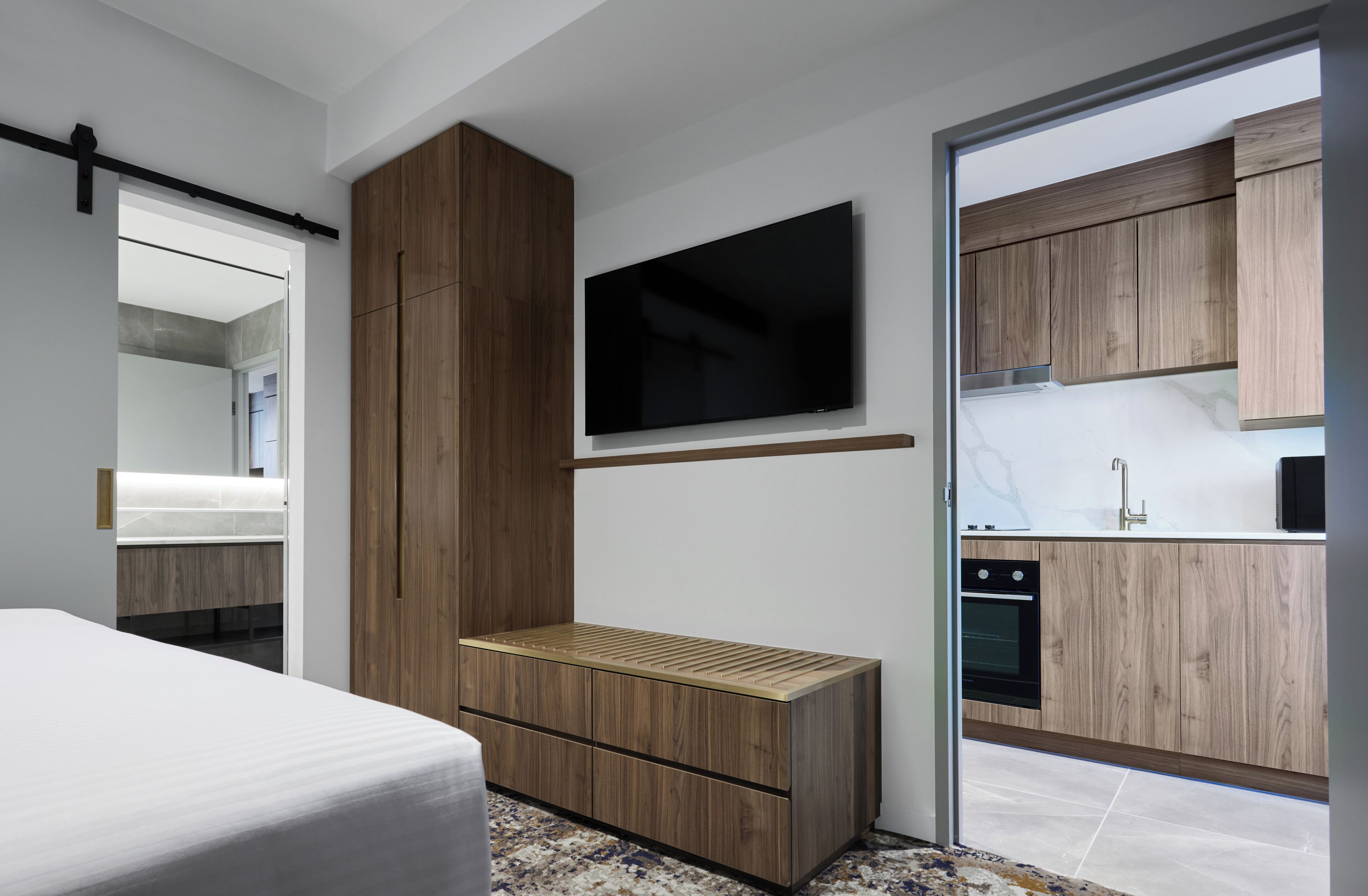 Une chambre à coucher moderne, avec un lit, un téléviseur fixé au mur et une porte coulissante donnant sur un espace cuisine.