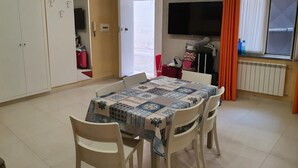 Un comedor con una mesa lista para cuatro personas, un televisor montado en la pared y una ventana con cortinas.