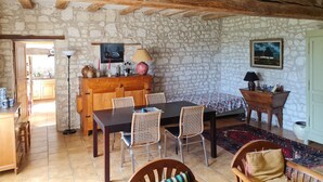 A rustic dining area with a stone wall, wooden beams, a tiled floor, and a wooden table with chairs. - Gîte "Chez Nicole" in the heart of the Loire castles (Restigné)