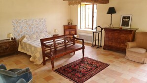 A cozy room with a bed, a wooden bench, a blue armchair, a patterned rug, and a dresser. - Gîte "Chez Nicole" in the heart of the Loire castles (Restigné)