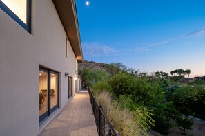 Ein modernes Gebäude mit großen Fenstern und einem Balkon mit Blick auf eine bepflanzte Grünfläche mit Bäumen und Sträuchern.