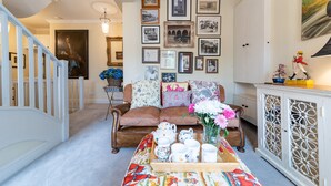 Un salon chaleureux avec un canapé marron, une table basse sur laquelle sont posées des tasses à thé, et un mur décoré de tableaux encadrés.