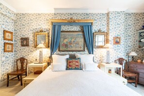 A bedroom with a large bed, a nightstand, a dresser, and a painting above the bed.