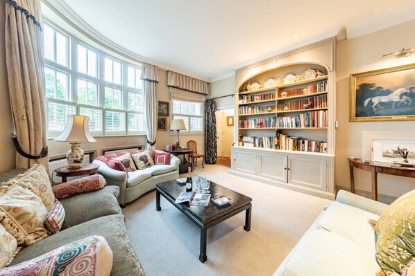 A spacious living room with a large bookshelf, comfortable seating, and large windows.