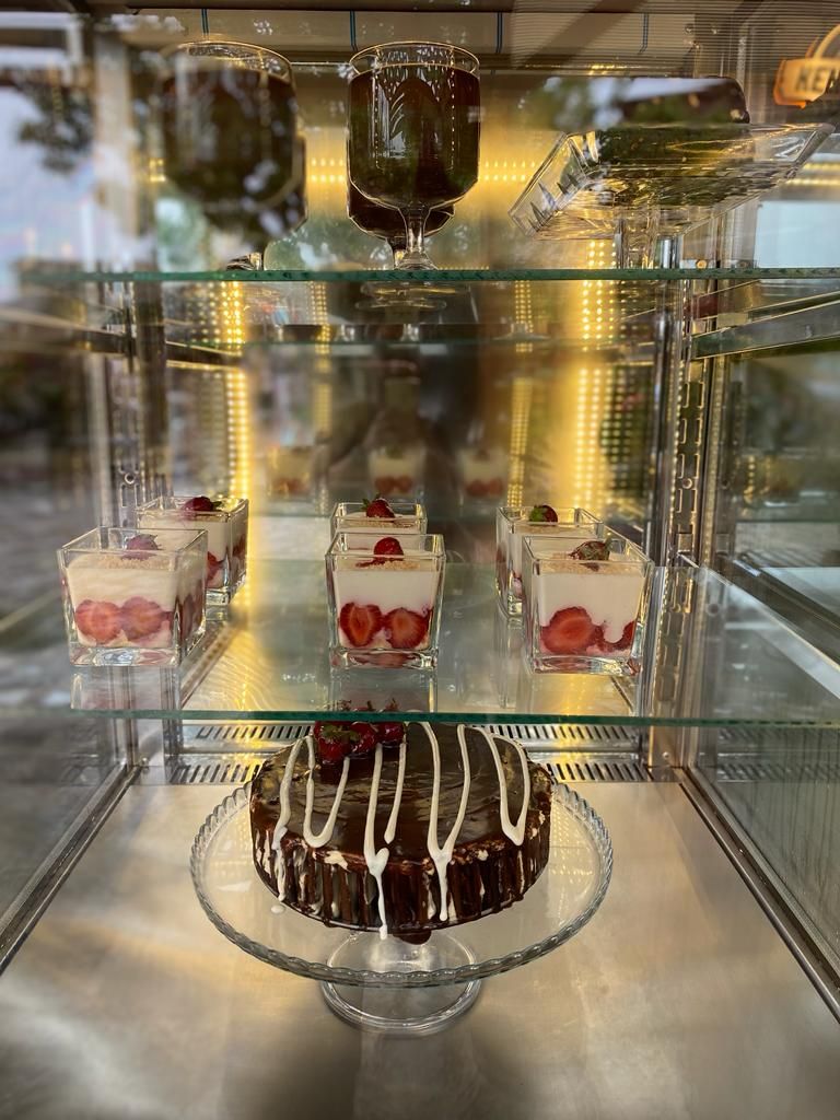 Een vitrine met desserts, waaronder verschillende lekkernijen en een taart op een glazen presentatieplateau.