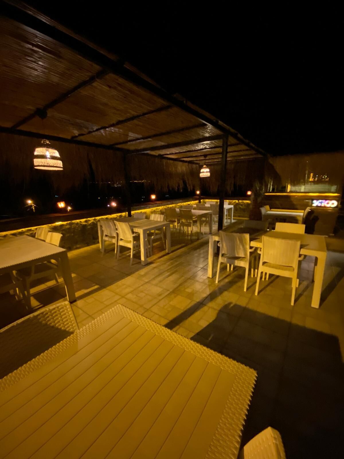 An outdoor patio area with tables and chairs, a thatched roof, and hanging lights.