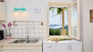 A kitchen with a sink, a clock, and a window with a view of greenery and a distant landscape.