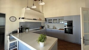 Une cuisine dotée d’un grand îlot central, de meubles blancs et d’une horloge au mur, avec une plante posée sur l’îlot.