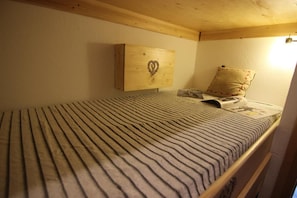 A single bed with a striped bedspread, a pillow, a magazine, and a wooden headboard with a heart design.